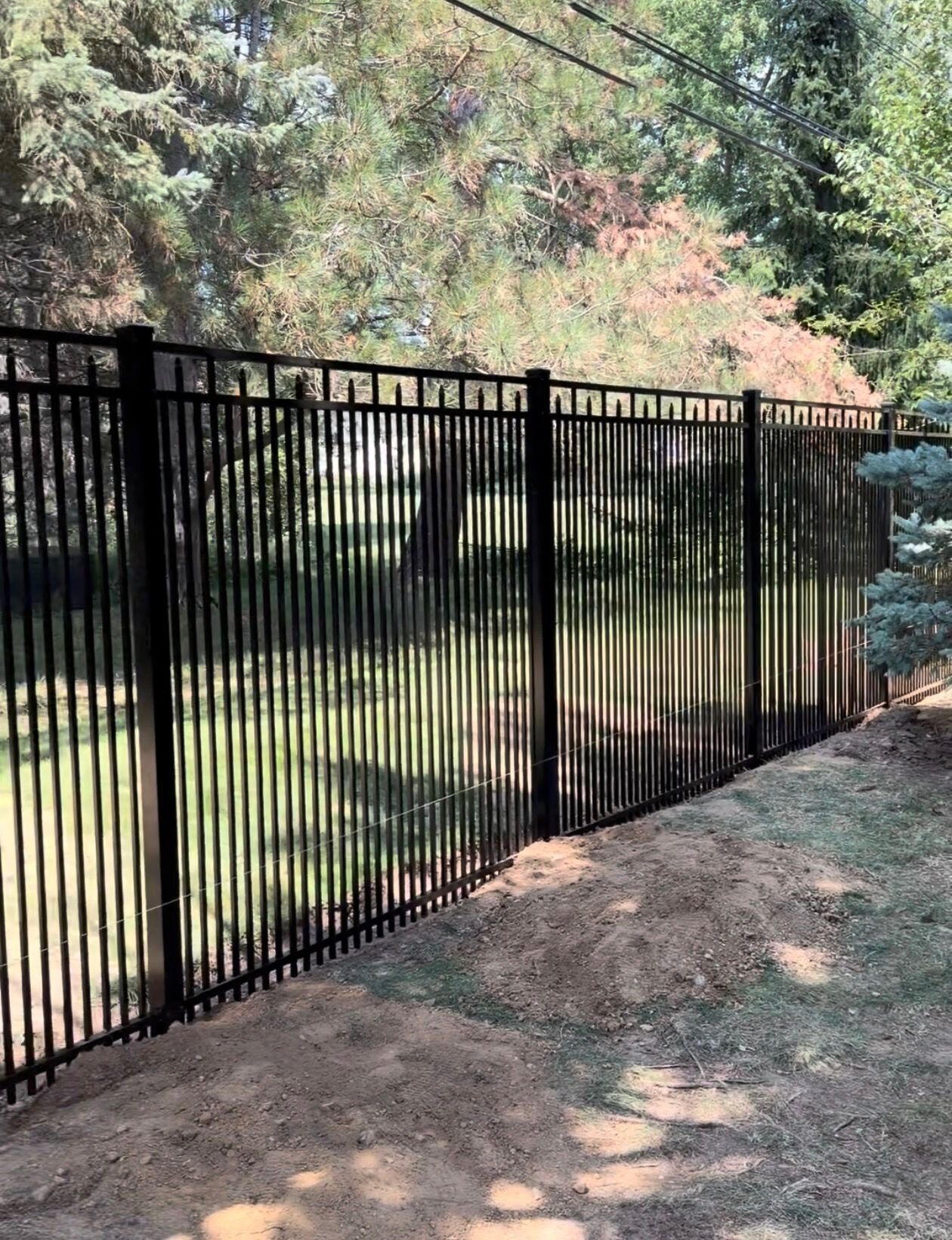 Black aluminum fence with spear-top pickets stepping down a sloped, wooded yard