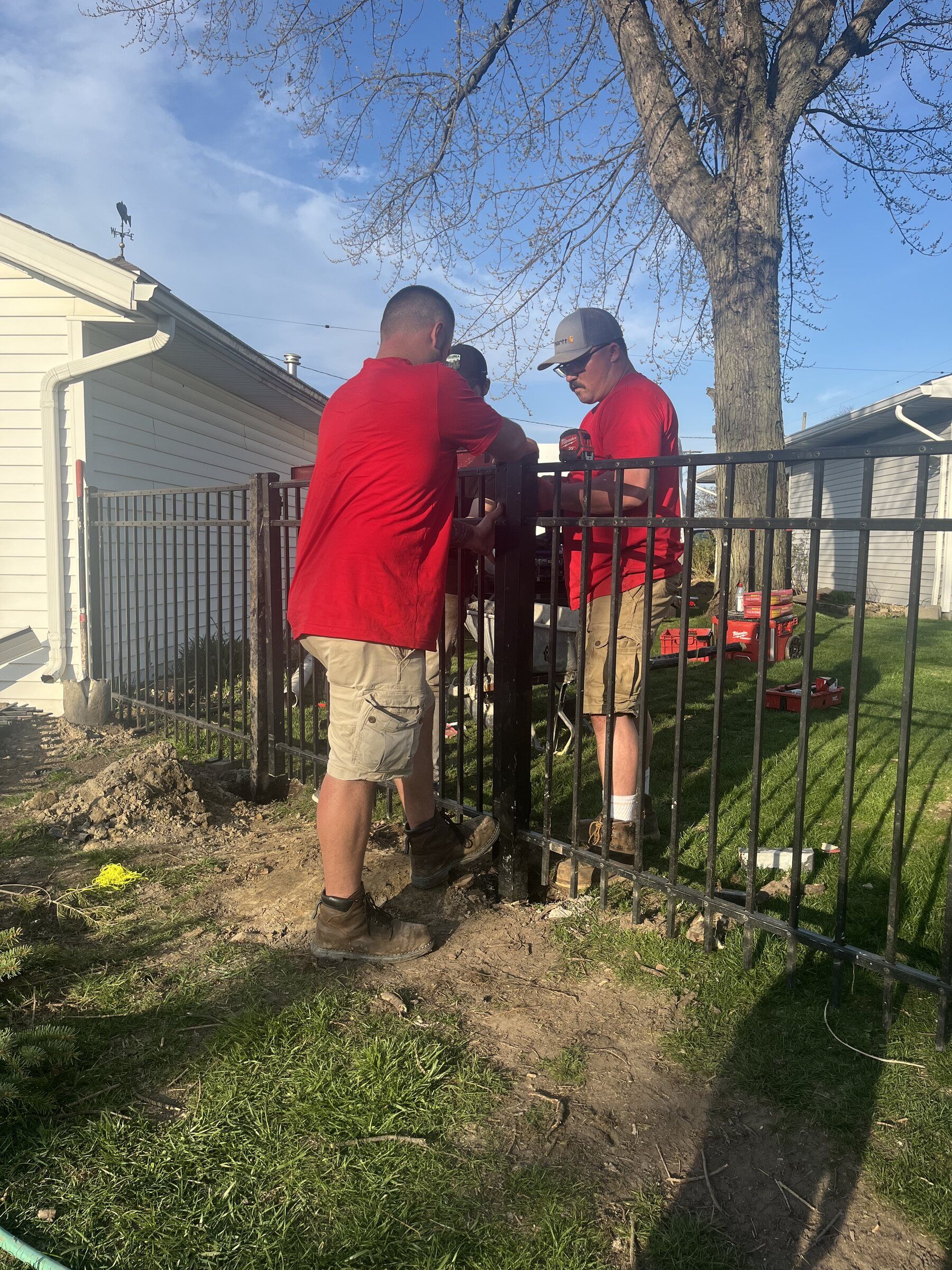 Two Final Touch Fencing crew members in red shirts installing a black aluminum fence