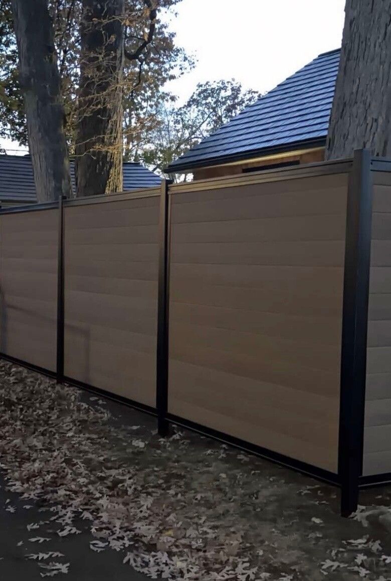 Wood-tone composite privacy fence panels framed by black posts along a paved path