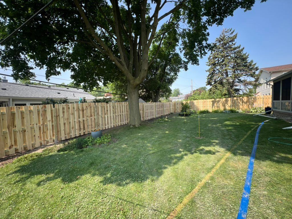 Wood privacy fence enclosing a large backyard lawn with a mature tree