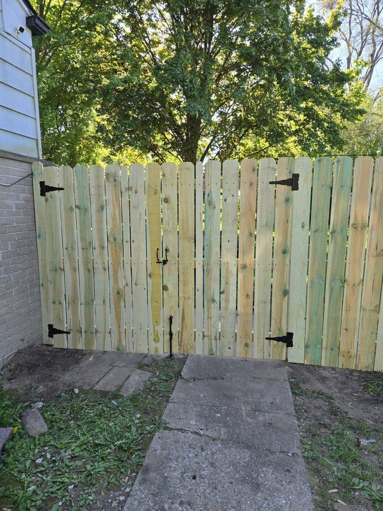 Wood privacy double gate with black hinges across a concrete walkway