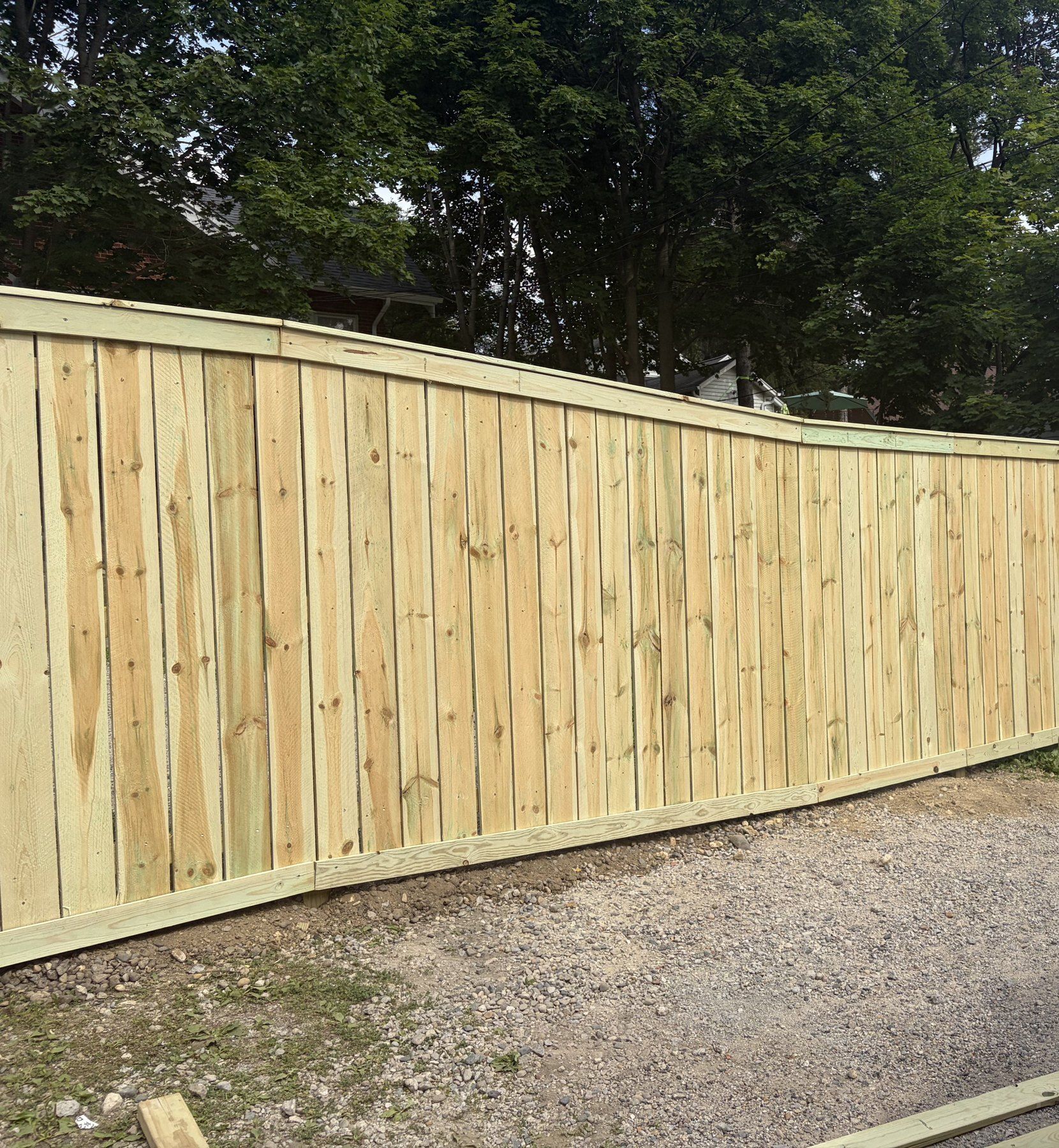 Long run of new wood privacy fence along a gravel drive
