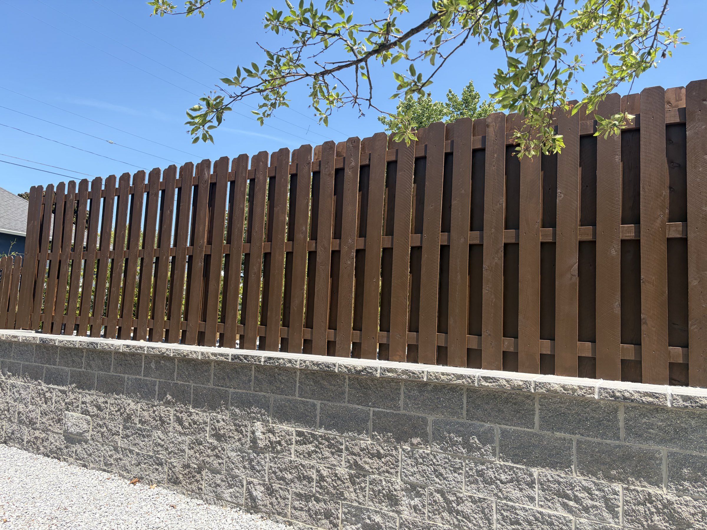 Dark brown stained shadow box fence on top of a block retaining wall